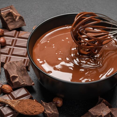 Schale mit flüssiger Schokolade und Schneebesen umringt von Schokoladenstücken